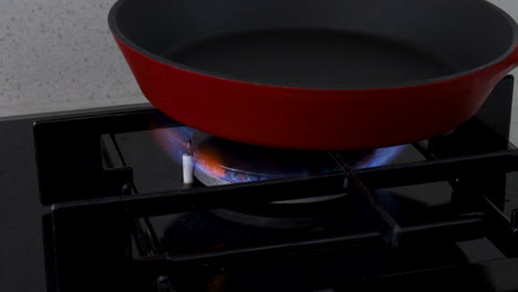 close-up of a red frying pan on a lit kitchen gas stove burner, ready for cooking, representing meal preparation and home cooking
