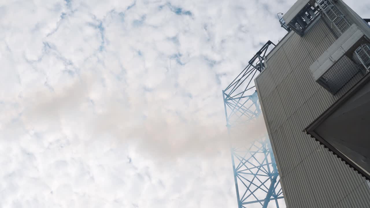 Grain dryer. White smoke from chimneys on cloudy sky background. Grain elevator. Metal building releases white vapor outdoors. Air pollution