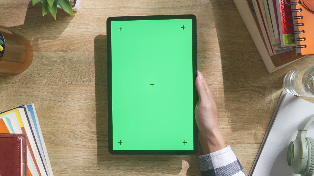 vista de arriba hacia abajo de una computadora portátil con pantalla verde simulada pantalla chromakey en un escritorio de oficina de madera al lado de la libreta con bolígrafos, gafas y un vaso de agua.