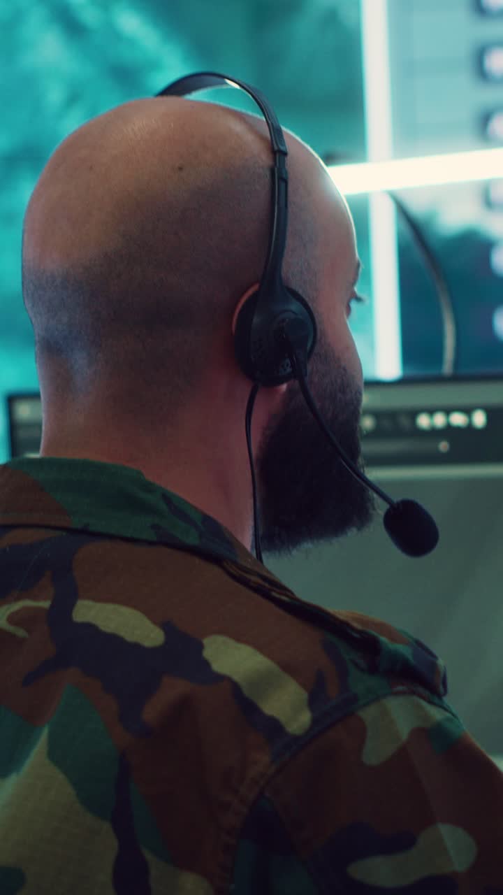 Mann i kamuflasjeuniform med headset som overvåker dataskjermer