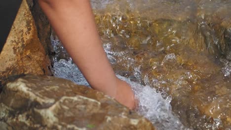 a hand dips into a stream of flowing water