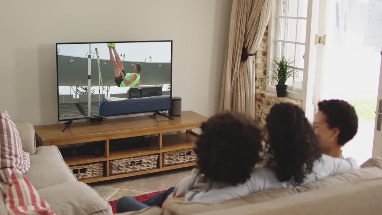 Famiglia felice seduta a casa insieme che guarda l'atletica salto in alto in TV
