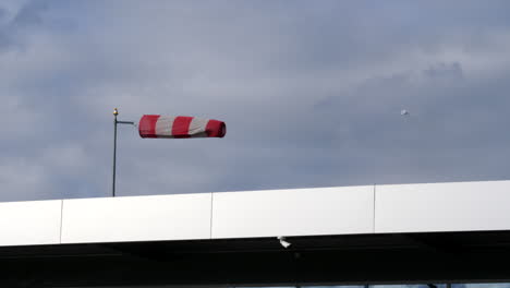 an isolated windsock blowing in strong winds at an airfield and an aircraft taking off in the background