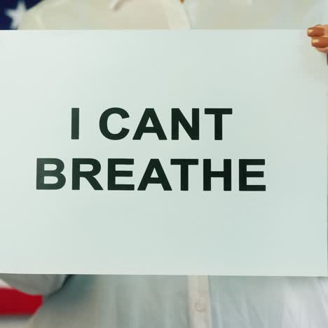 woman holds poster stating i cant breathe on american flag background