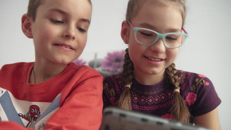 smiling childrens looking at mobile phone. boy and girl watching cartoon at home