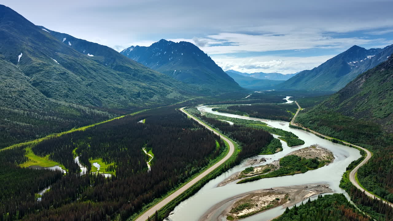 Valley among the spectacular mountain is overgrown with pine tree woods. A branching river is crossing the landscape. Aerial view. Alaska, USA