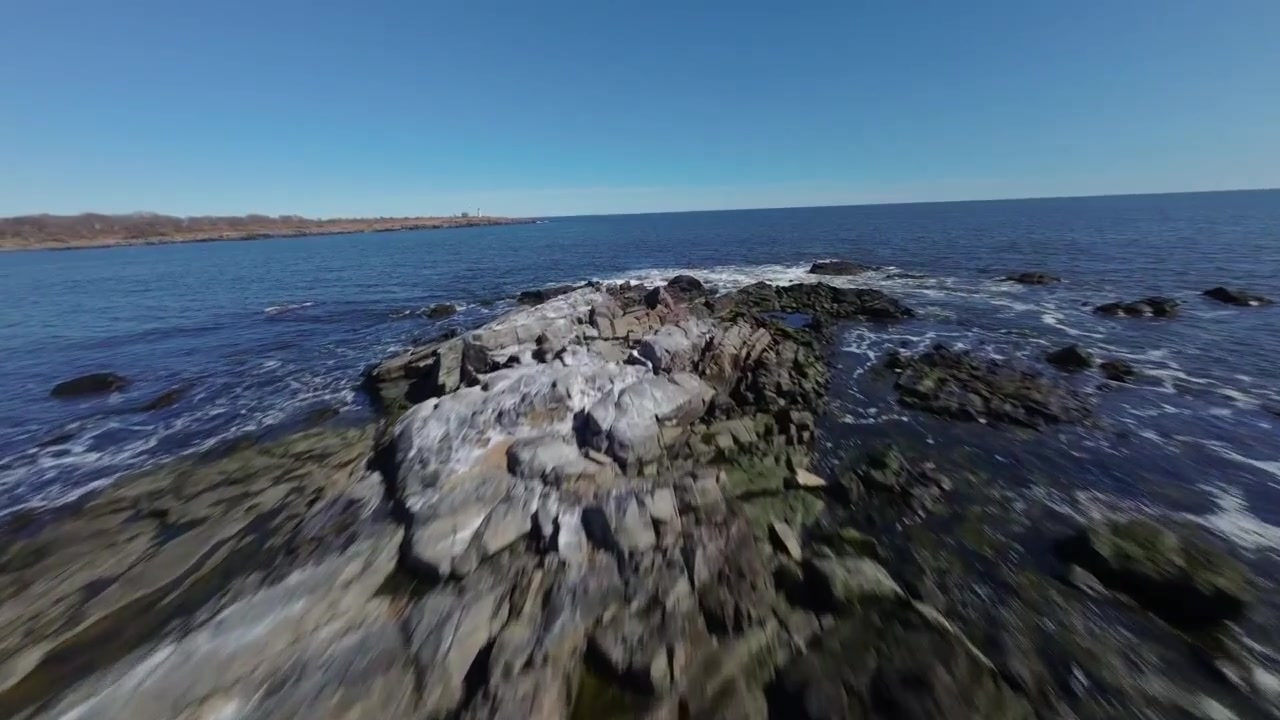 Ripresa con drone FPV che sfreccia sopra una piccola massa terrestre rocciosa circondata da scintillanti acque costiere lungo la frastagliata costa del New Hampshire