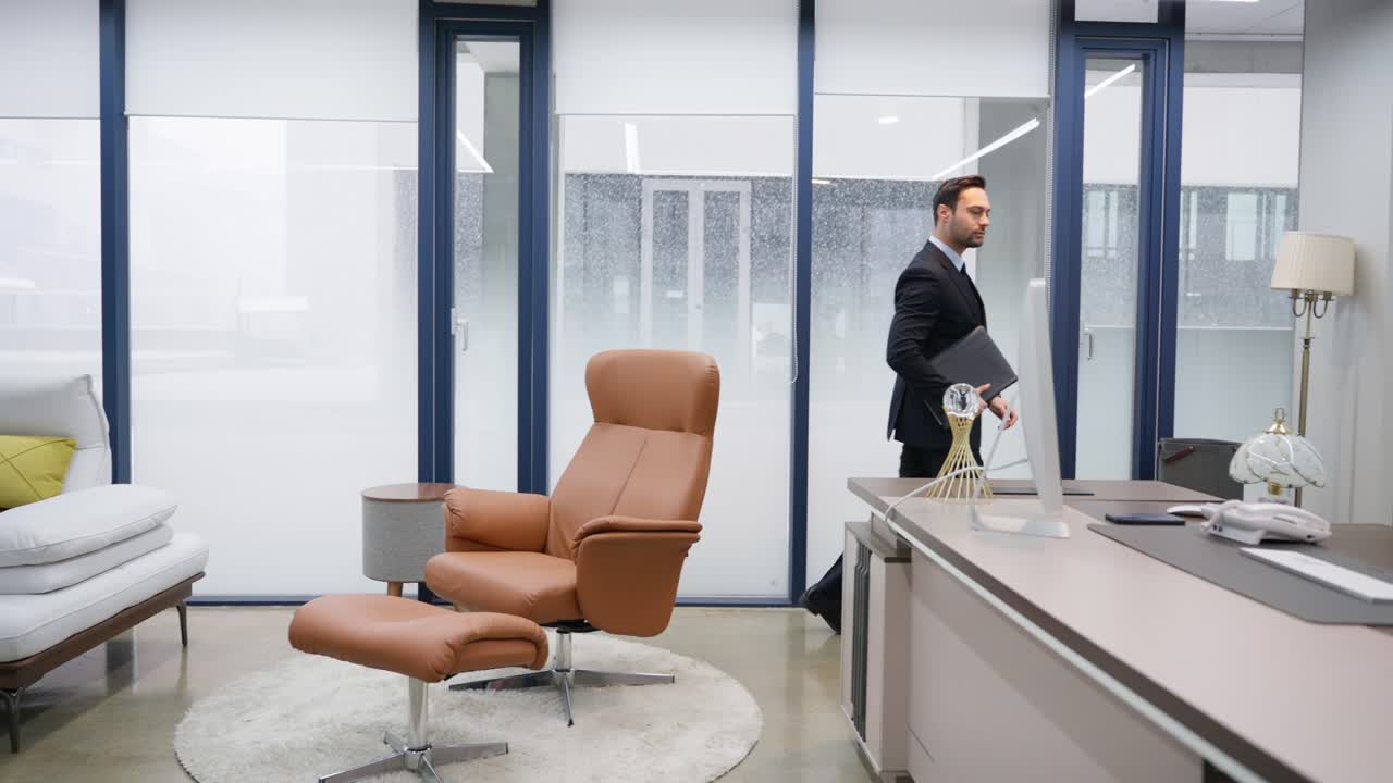 Tracking shot of French Businessman executive walks to desk, sits in an armchair and reviews business paper documents in luxury office