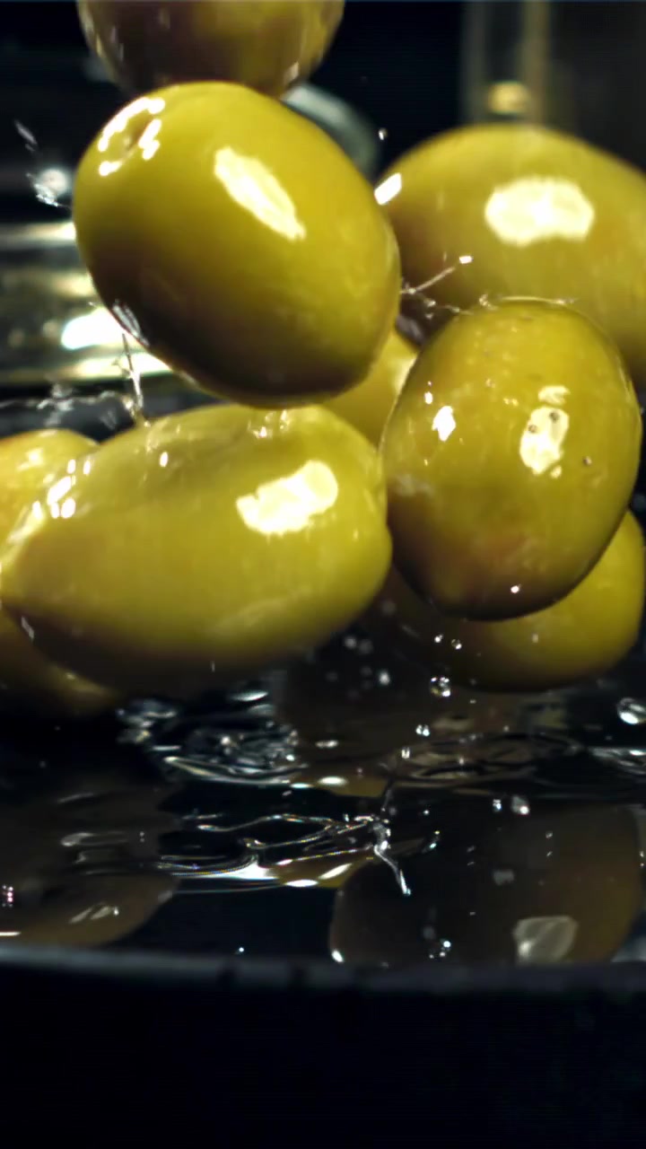 Olive verdi fresche che schizzano nel liquido al rallentatore