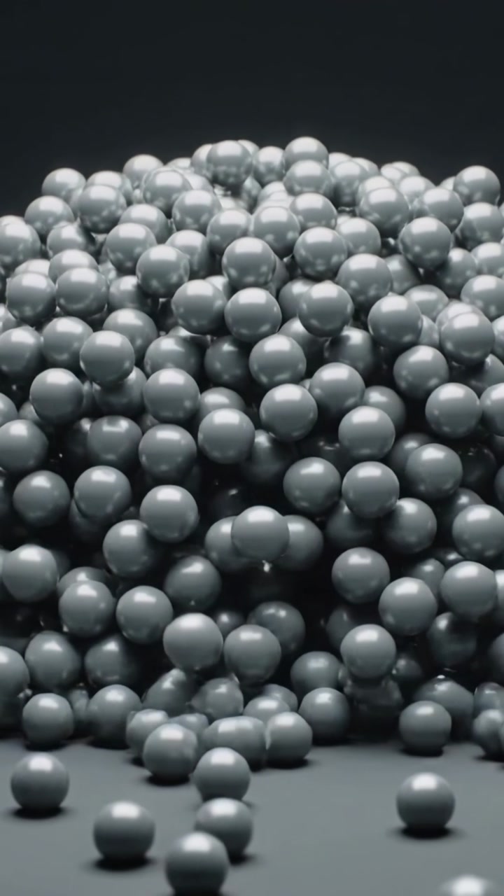 Vertical video: Falling metal spheres hitting and forming dense heap on flat table under top light