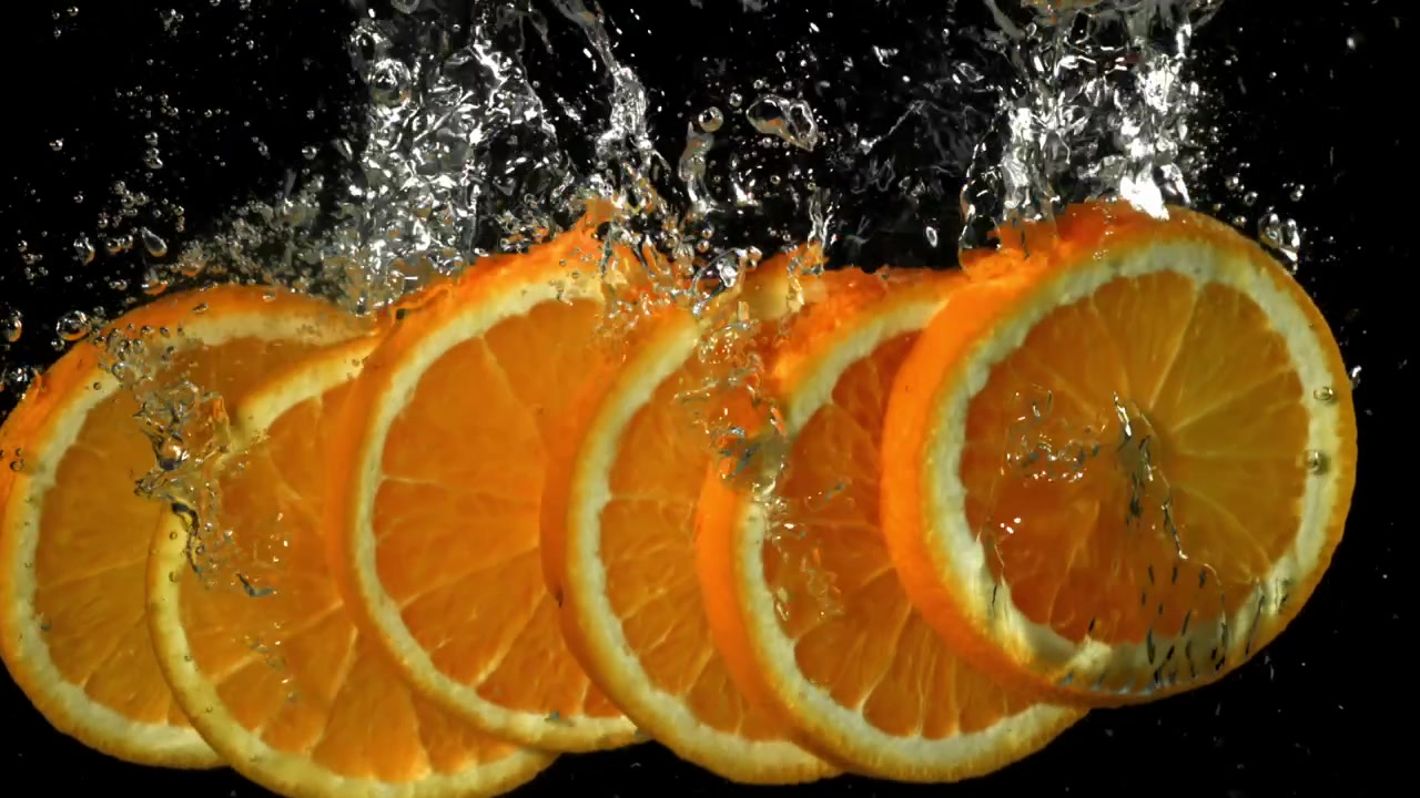 Fette d'arancia fresche che schizzano nell'acqua su sfondo nero.