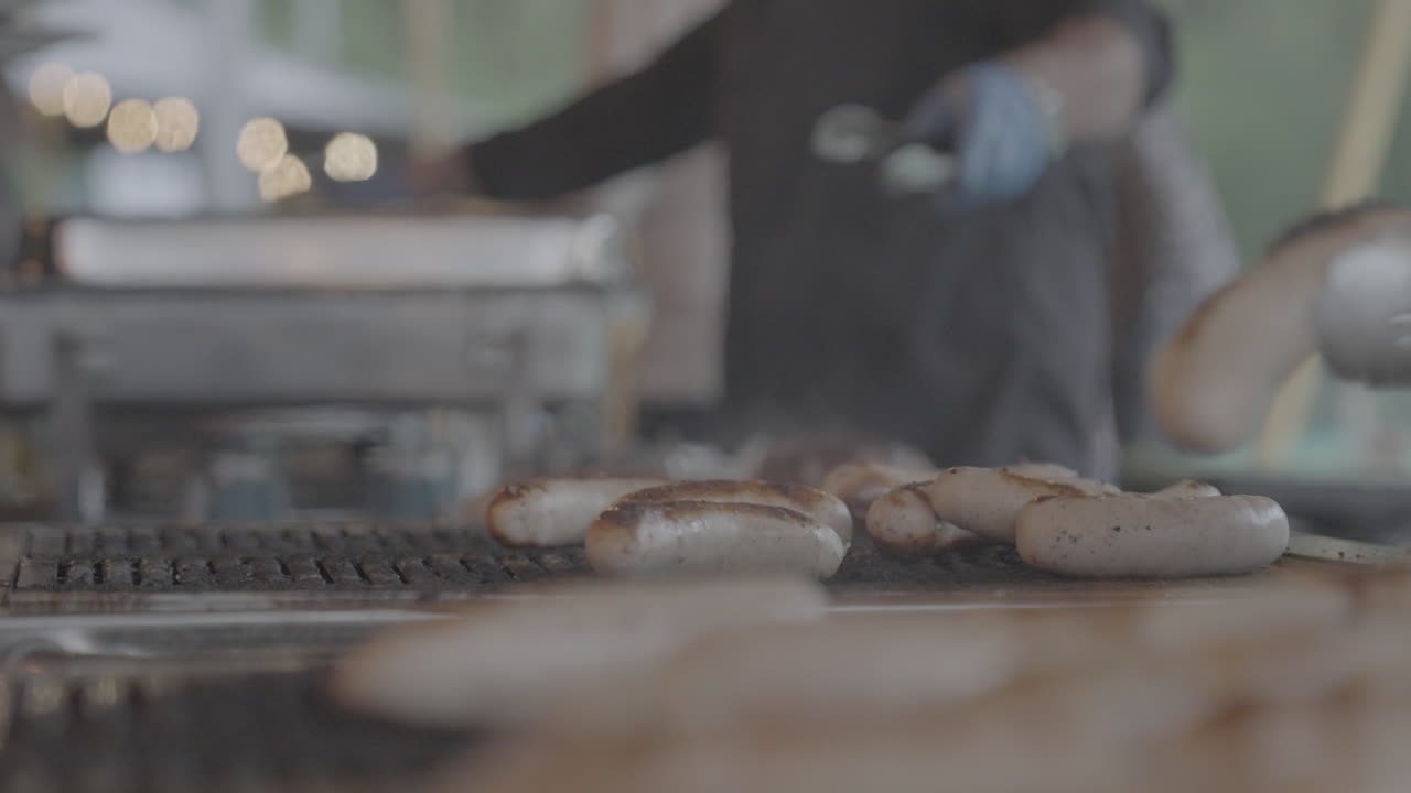 Baking and grilling sausages on a smoking barbecue grill and flipping them over in slowmotion with a focus shift from back to front LOG