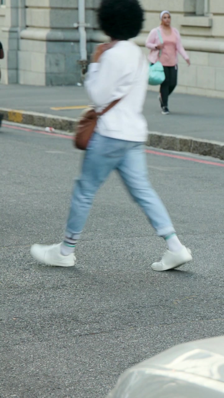 Vertical video: Walking woman in pink top and hijab entering frame, moving along curb with teal bag