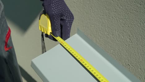 worker hands in protective gloves checking pvc window metal sill size with measuring tape closeup