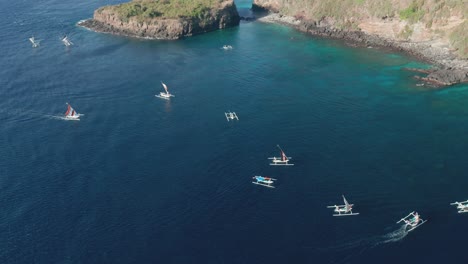 wooden cadik fishing boats moving in blue water towards rocky shore of bali, aerial