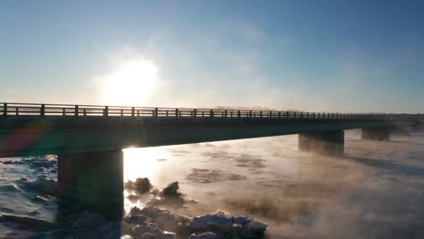 winter wonderland with a snowing cold river, clear skies, and misty fog rolling over the kenai river in alaska with mountains in the background.