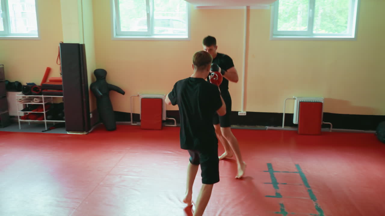 Two wrestlers sparring in gym on red mat, practicing martial arts with gloves, barefoot, exchanging punches, focusing on combat training, power, endurance, agility, discipline, balance, coordination