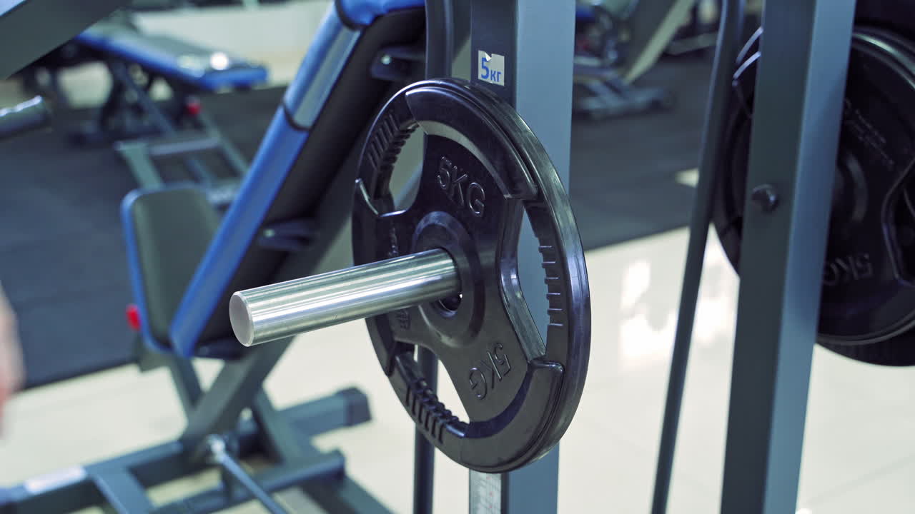 Athletic woman with slim body in blue shorts is putting disk to the barbell. Sports gym background and a young woman training.