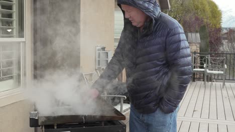 hombre limpiando una plancha superior plana después de un cocinero al aire libre - vapor subiendo en cámara lenta