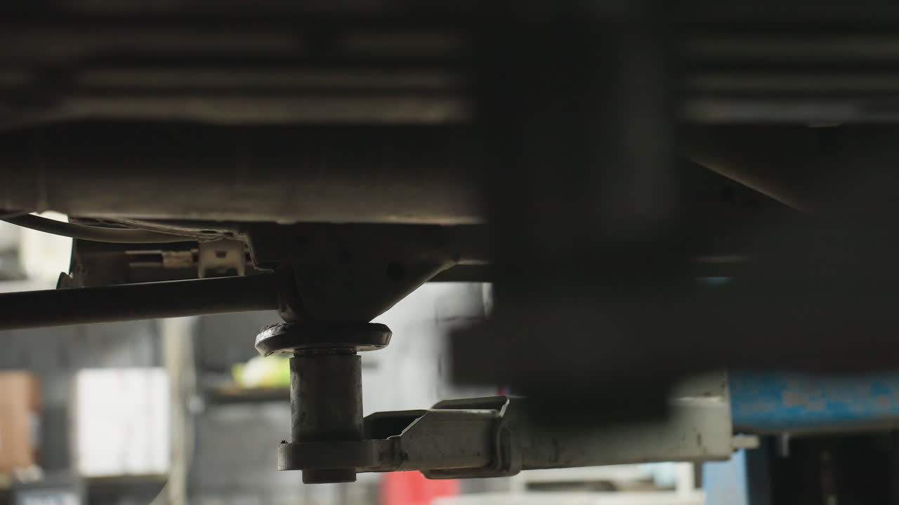 Close-up of car lift supporting vehicle in workshop with blurred background featuring mechanical equipment, tools, and garage elements