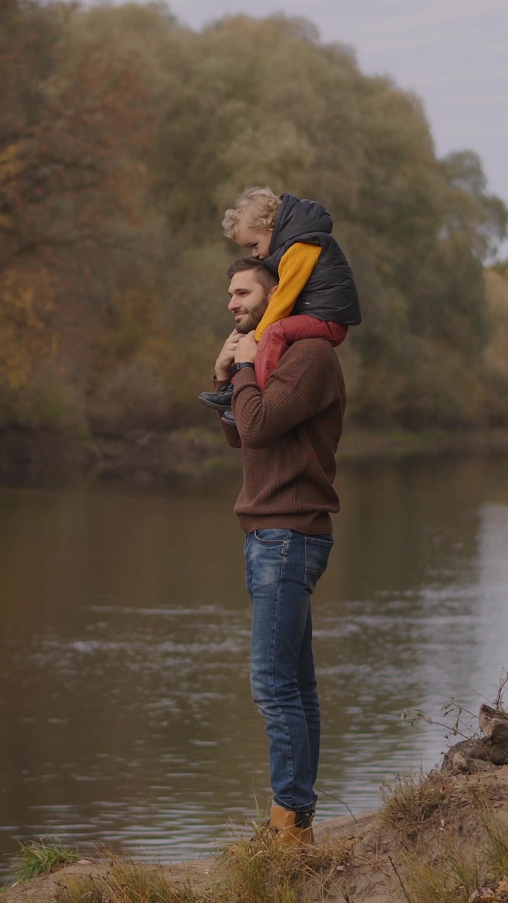 Padre che porta il figlio piccolo sulle spalle in riva al fiume