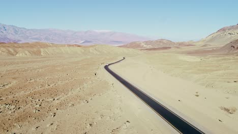 a lone white car moves along black asphalt road, death valley desert, clear sky