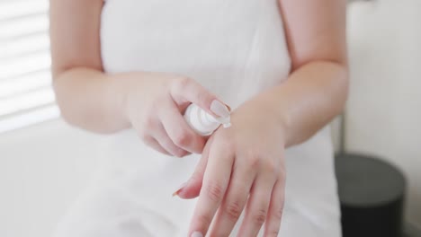 caucasian plus size woman with bathrobe putting cream on hand in slow motion