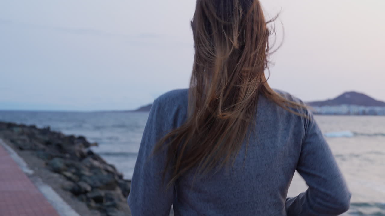 woman jogging on Las Canteras beach at sunrise with her hair blowing in the wind, Las Palmas de Gran Canaria