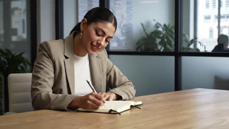 a professional woman engaged in writing notes at her desk in a sleek office environment, radiating confidence and focus