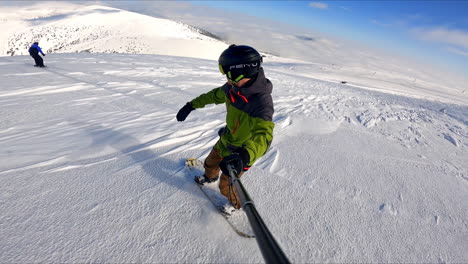 sportsman with a selfie stick rides down the slope on his snowboard. winter sport activity.