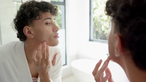 applying skincare, non binary person examining face in bathroom mirror, focusing on skin