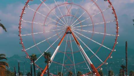 ferris wheel against the blue sky with clouds near the palm trees in the resort town, sunny day