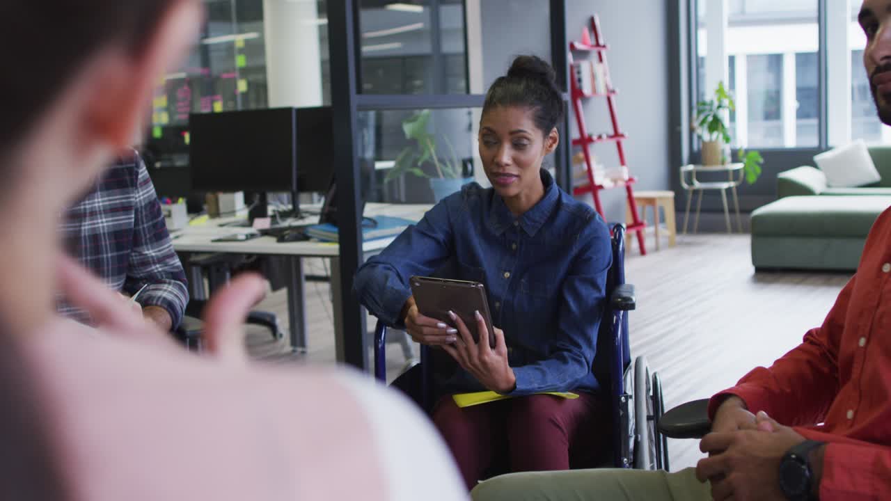 Mixed race businesswoman sitting in wheelchair discussing with diverse group of colleagues