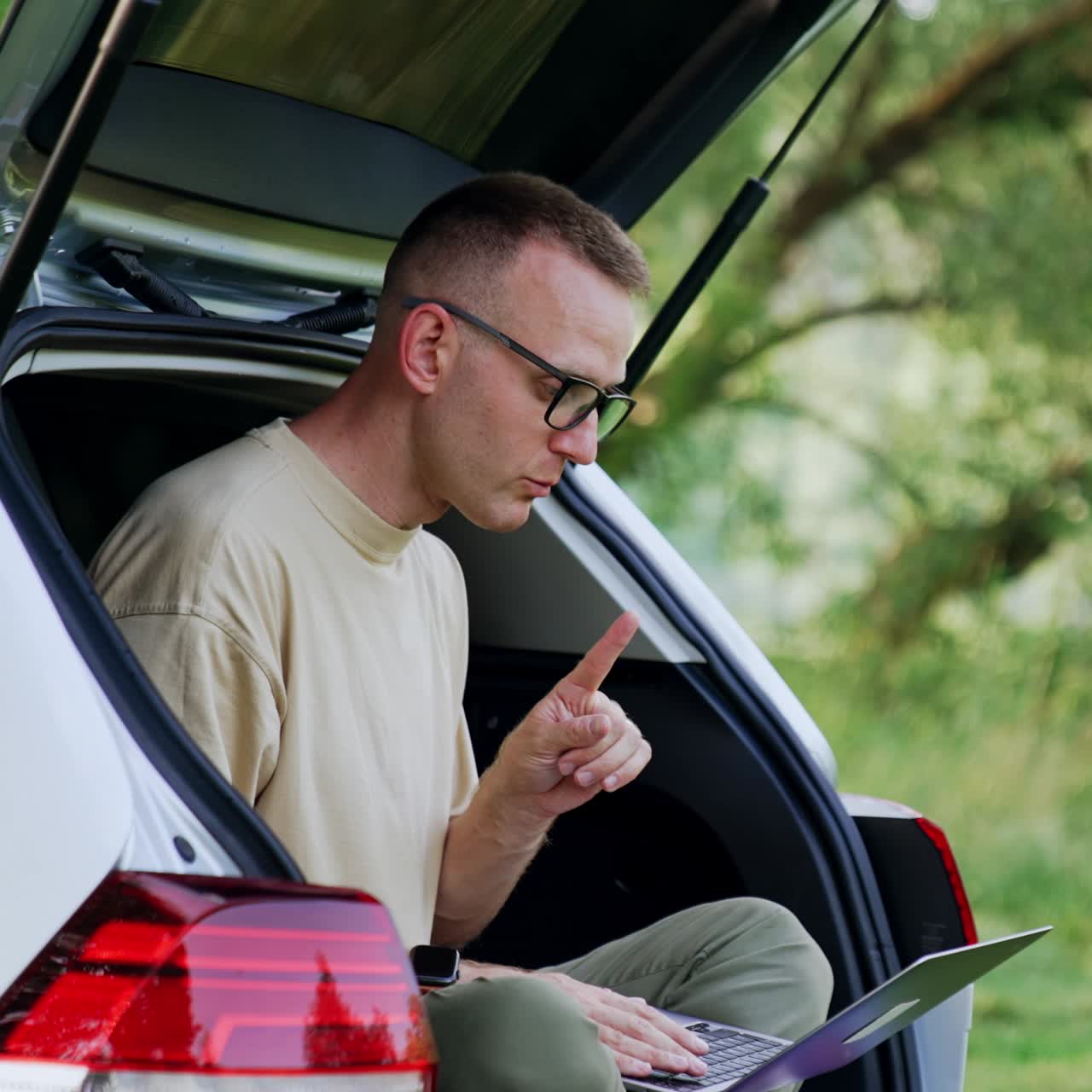 Working in nature. Man in glasses types on his laptop, speaking to himself. Freelance concept