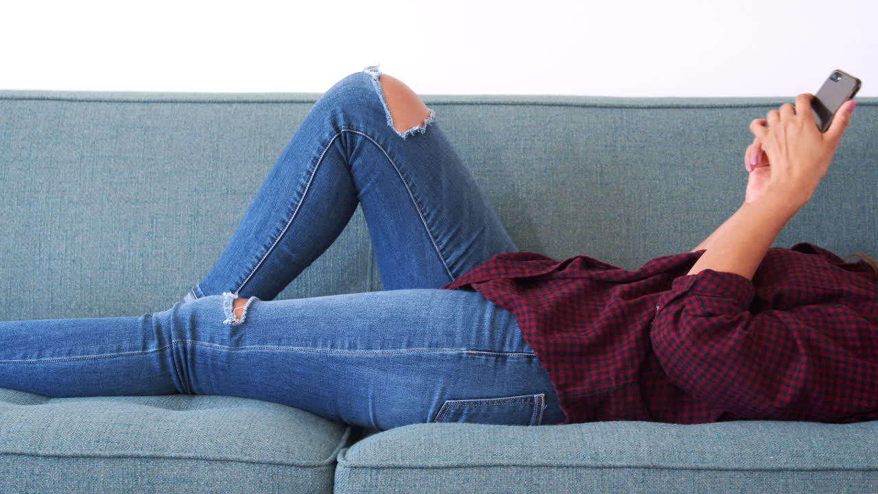 가정 에서 휴대 전화 를 사용 하고 소파 에 누워 있는 여자
