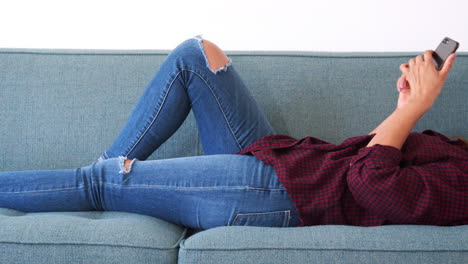 mujer acostada en el sofá en casa usando el teléfono móvil