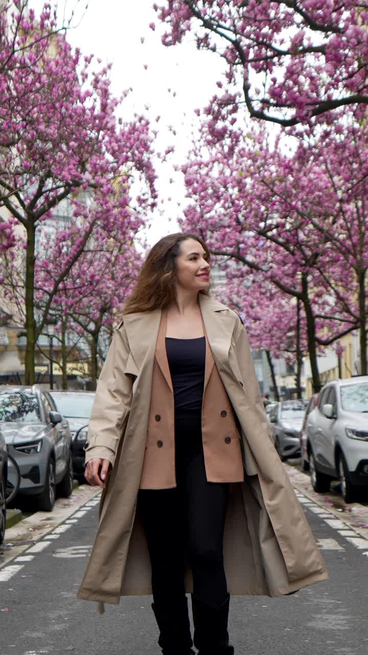Donna felice che cammina per una strada cittadina costeggiata da alberi di magnolia in fiore.