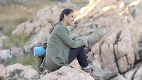 Sitting on rocky terrain, woman enjoying nature during mountain hike with yoga mat