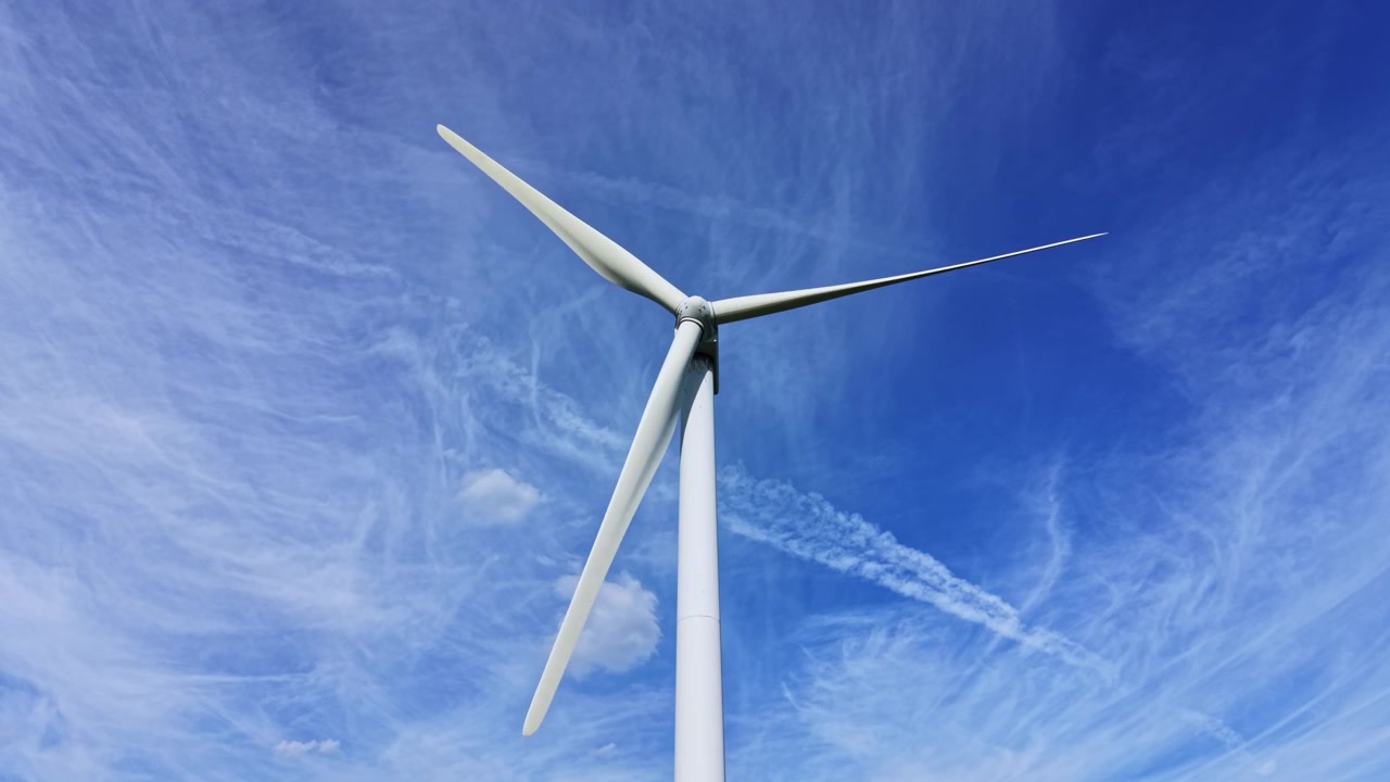 Una turbina eolica si staglia imponente contro il cielo azzurro con nuvole, di giorno, in un paesaggio di energia rinnovabile.
