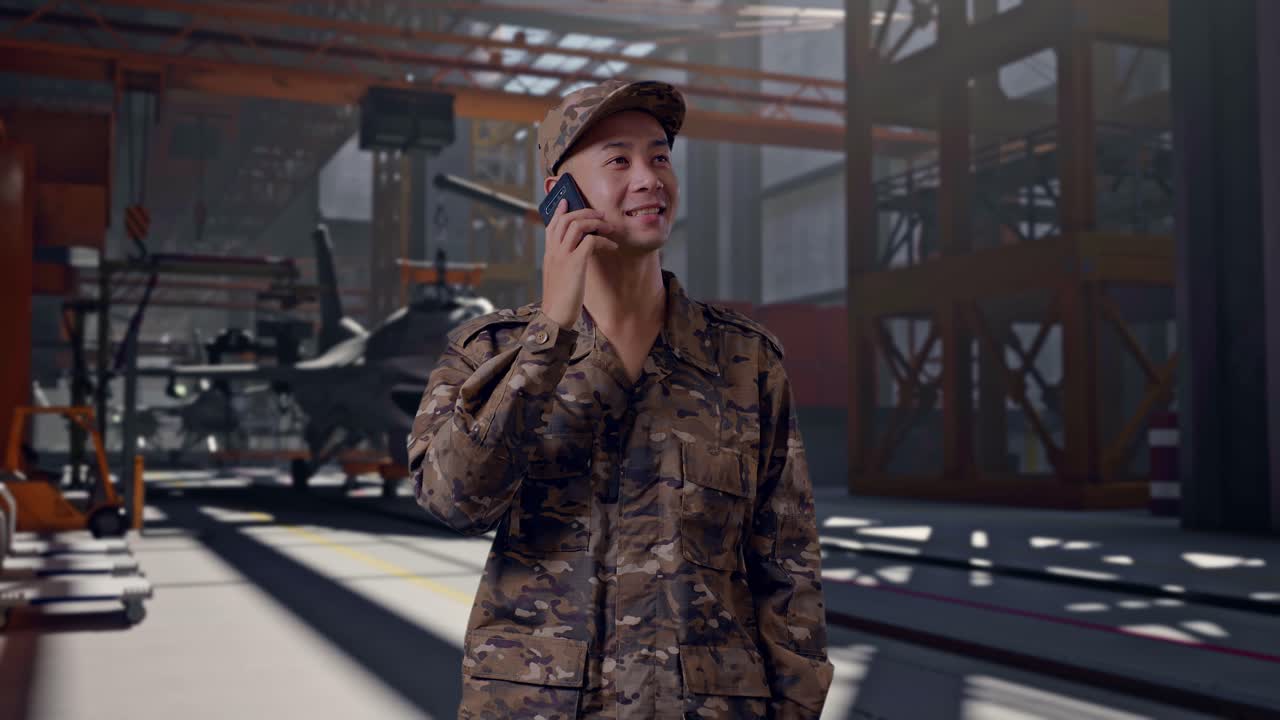 Fröhlicher Soldat in Camouflage-Uniform, der in einem Hangar mit einem Smartphone telefoniert