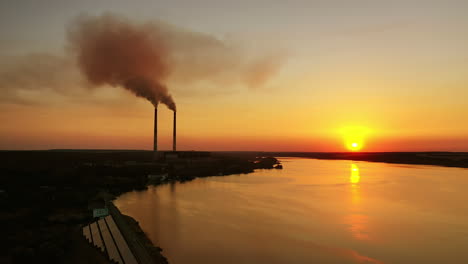 orange sunset over the water. harmful plant with industrial pipes near the river. dirty emissions pollute the air in the evening.