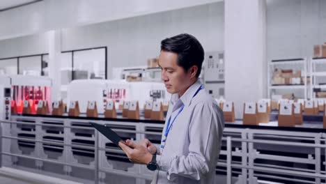 side view of an asian male professional worker standing with his tablet with conveyor for packaging coffee beans in bags at coffee factory, checking on his tablet with meditation