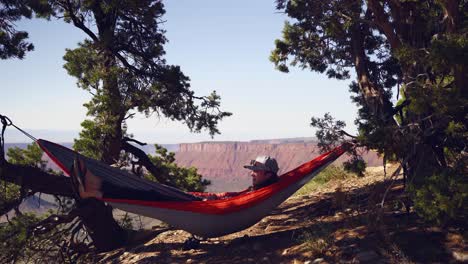 young man enjoys hammock in tree shade overlooking deep utah canyon