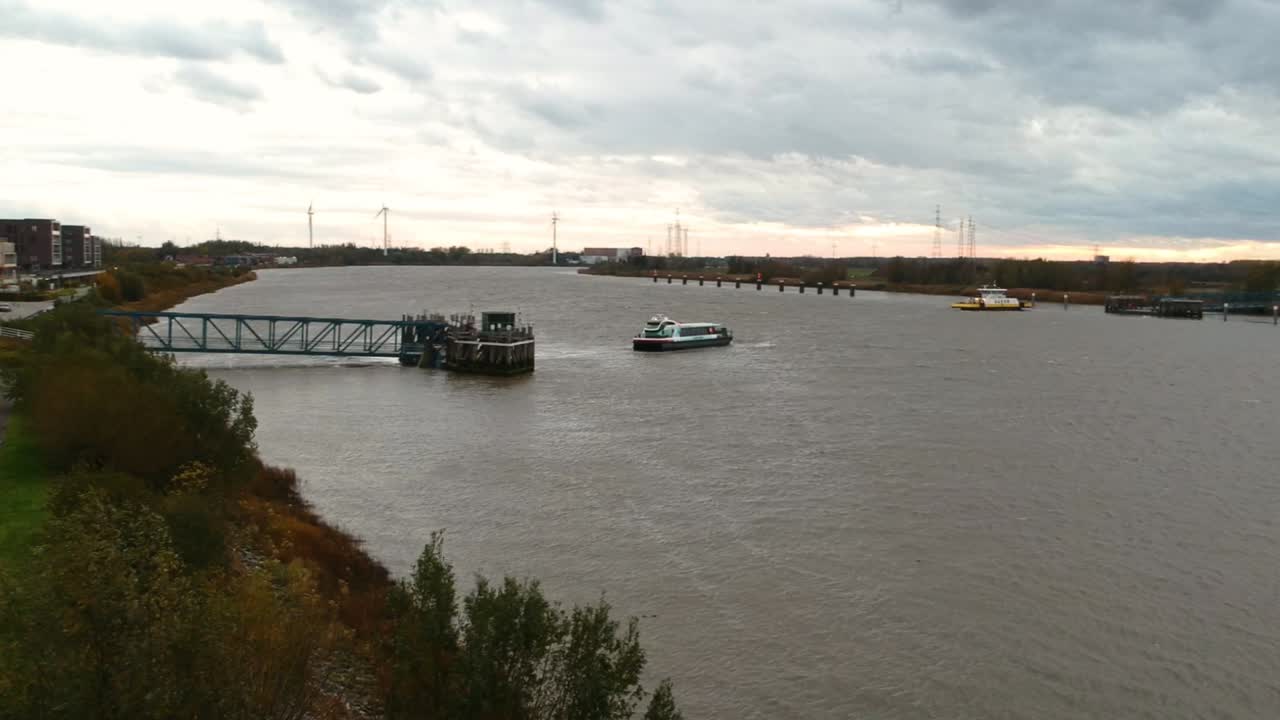 дрон отъезжает назад над рекой с паромом с серым пасмурным горизонтом