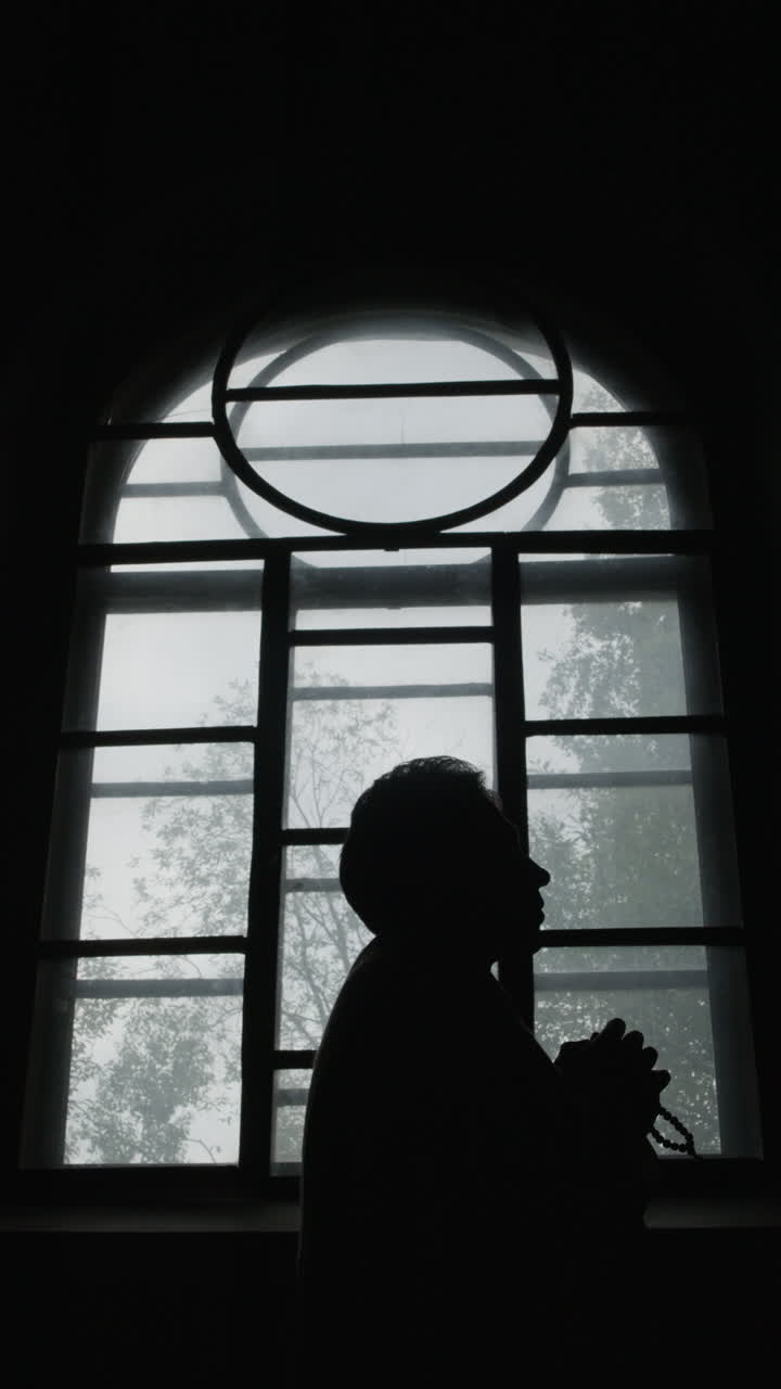 Silhouette of a Person Praying by a Window