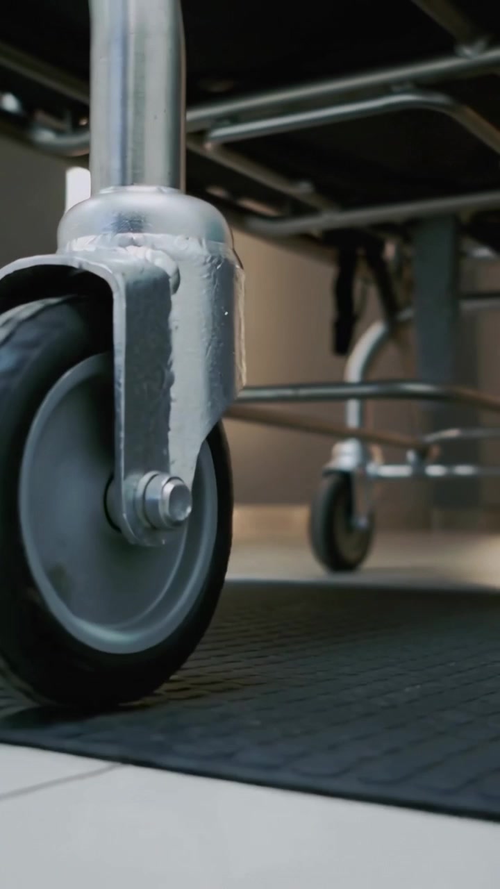Vertical video: Rolling caster wheel mounted on cart after push across tile floor, showing welds
