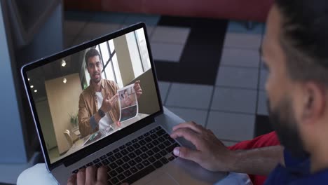 hombre de oriente medio teniendo una videollamada con un colega de oficina masculino en una computadora portátil