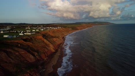 aerial drone 4k video flies over the cliffs of isle of wight towards grange farm campsite with lots of campervans and tents during the golden hour light of sunset