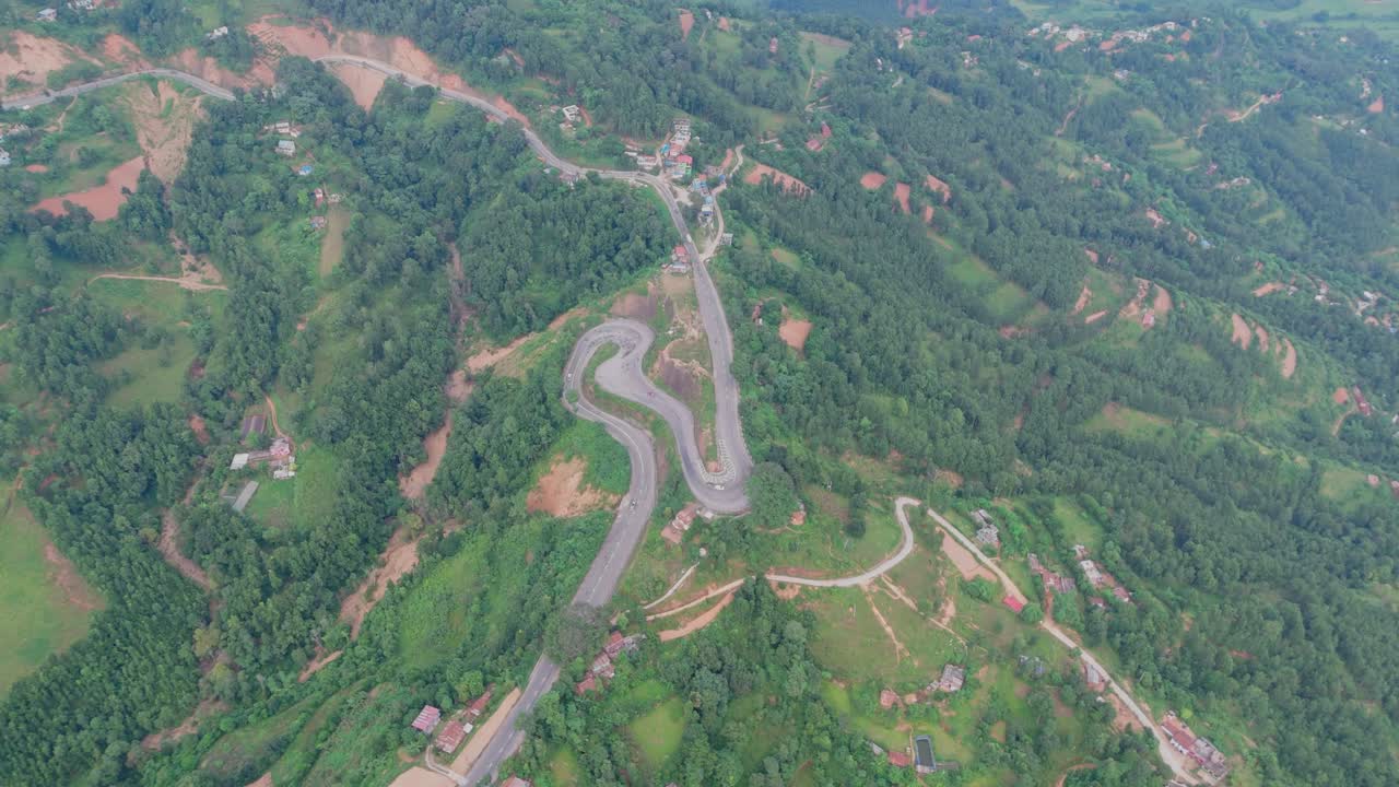 Aerial view of a vehicle driving along a winding hillside road surrounded by lush green mountains, showcasing scenic mountain travel, nature, and rural transportation beauty