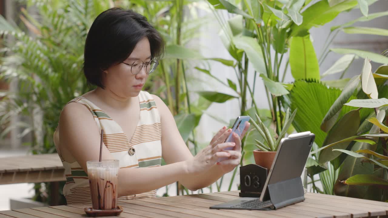 카페에 앉아 여행을 찾기 위해 온라인 쇼핑과 소셜 미디어에서 터치 스마트폰을 사용하는 여성 짧은 머리카락, 안경을 입은 관광객.
